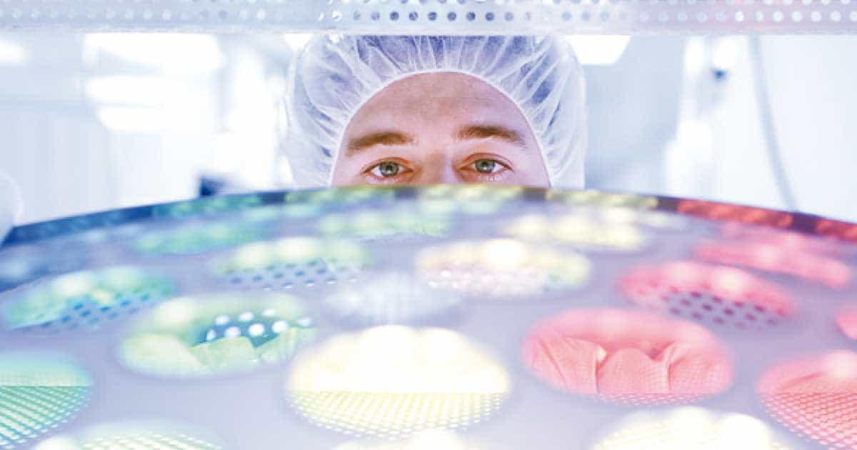 Ein Mann in einem Laborkittel betrachtet ein buntes Licht.