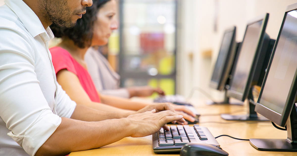 Mehrere Personen sitzen an einem Schreibtisch und arbeiten an ihren Computern