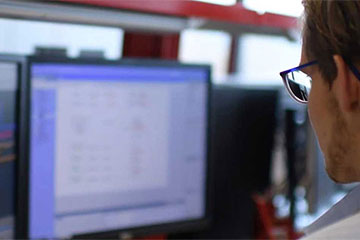 Ein Mann mit Brille arbeitet an zwei Computerbildschirme.