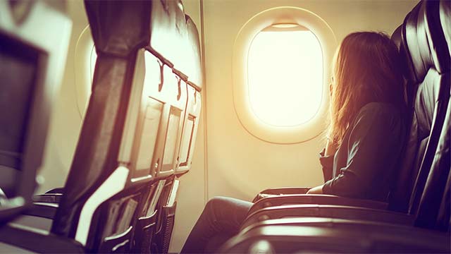 Eine Frau sitzt in einem Flugzeug und schaut zum Fenster raus