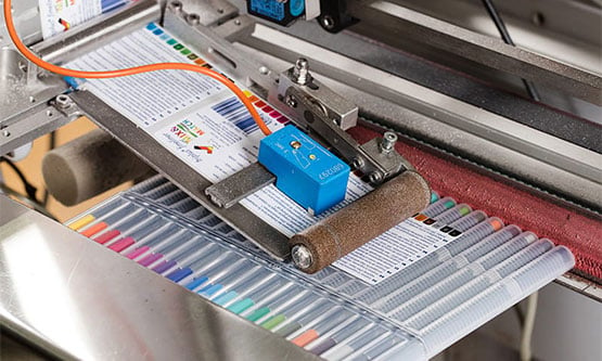 Nahaufnahme einer Maschine, die Etiketten auf Verpackungen von Stiften anbringt