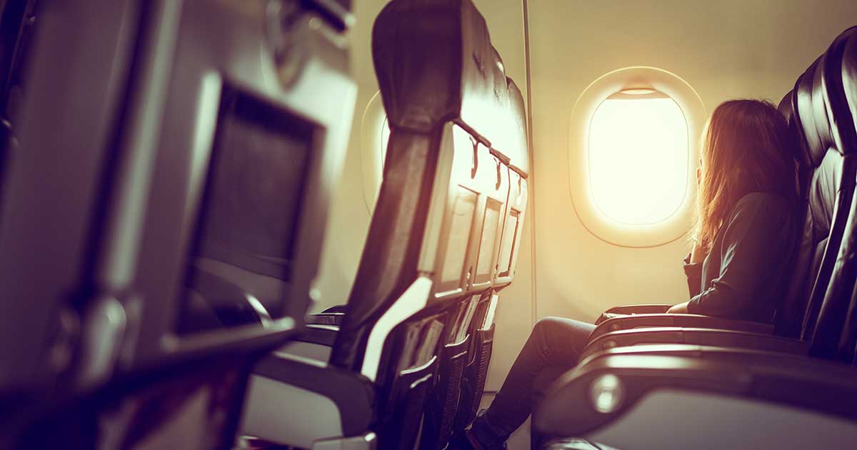 Eine Person sitzt im Flugzeug, die Sonne scheint durch das Fenster.