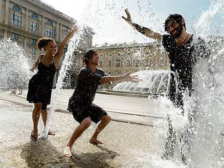 Drei erwachsenen Personen spielen mit Wasser neben einem Brunnen