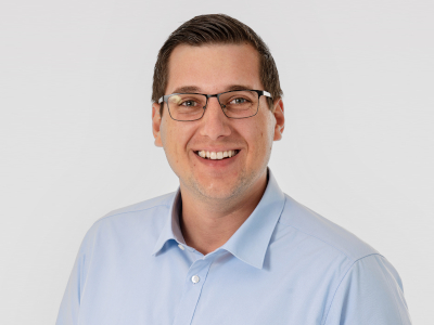 Laechelnder Mann mit Brille im hellblauen Hemd